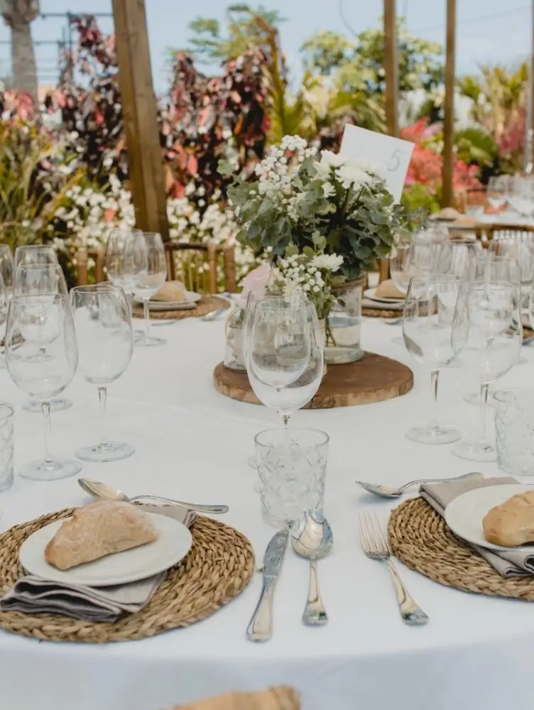 Mesa redonda vestida con mantelería natural, vaixela rústica e flores brancas, banquete elegante Cinza e Lume.
