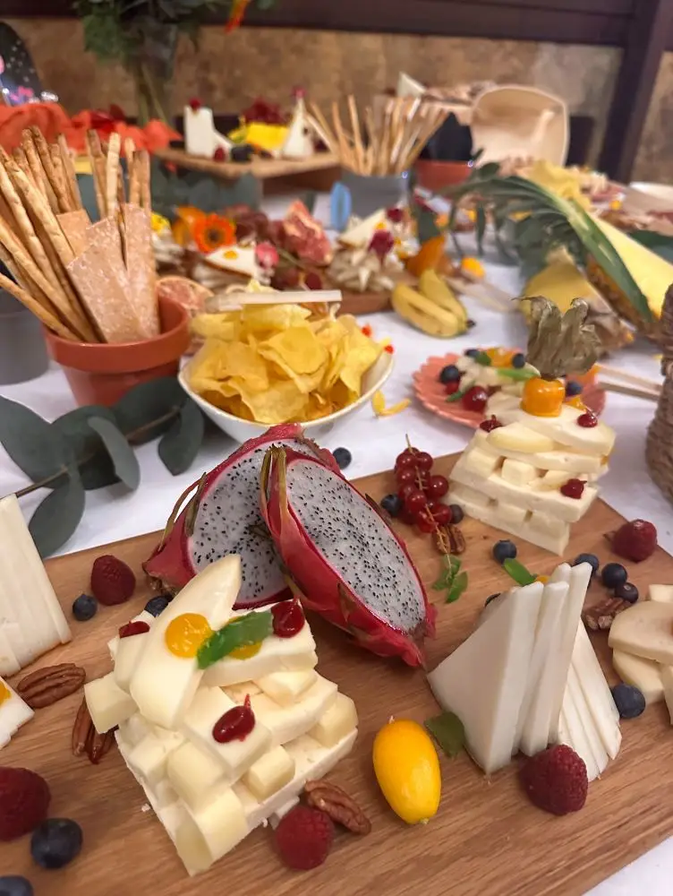 Mesa rústica con froitas tropicais, queixos e decoración natural, estación temática de catering Cinza e Lume.