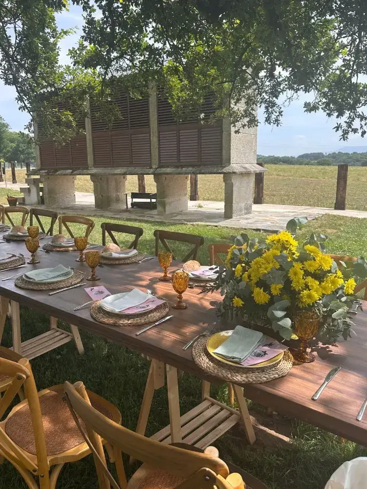 Mesa exterior con mantelería branca e centros florais amarelos, montaxe de banquete ao aire libre Cinza e Lume.